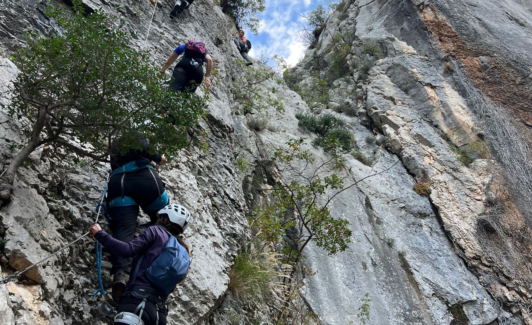Group of climbers clipped to the cable on a steep limestone via ferrata, in helmets and harnesses