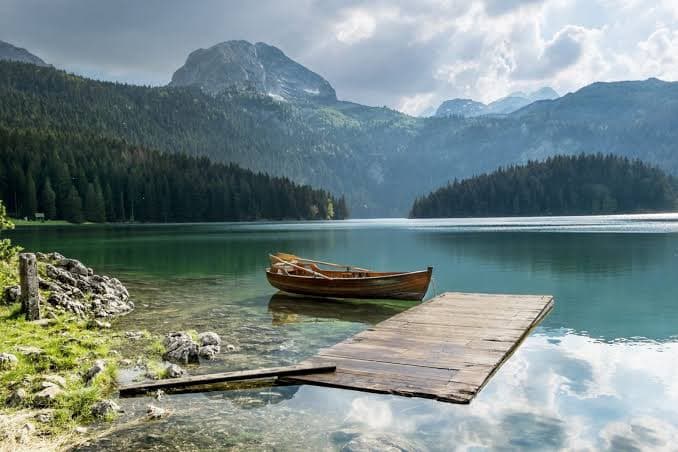 Wooden jetty and a rowing boat on a still mountain lake below forested peaks in Montenegro