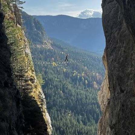 A walker crossing a cable strung between two limestone cliffs above the forested Romanija valley