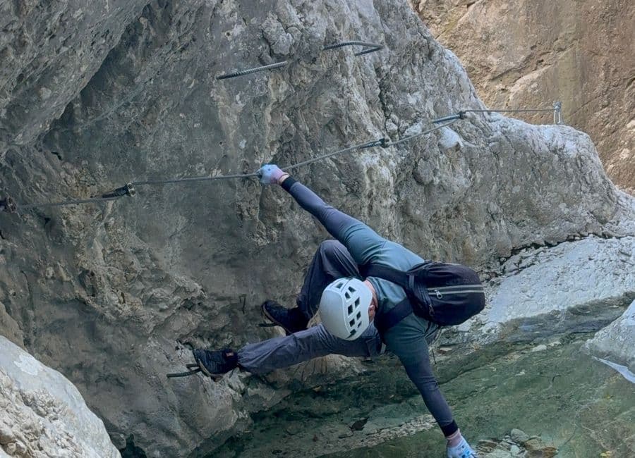 Climber traversing the cable above a green pool in the Podružje canyon on the Ilirski Put route