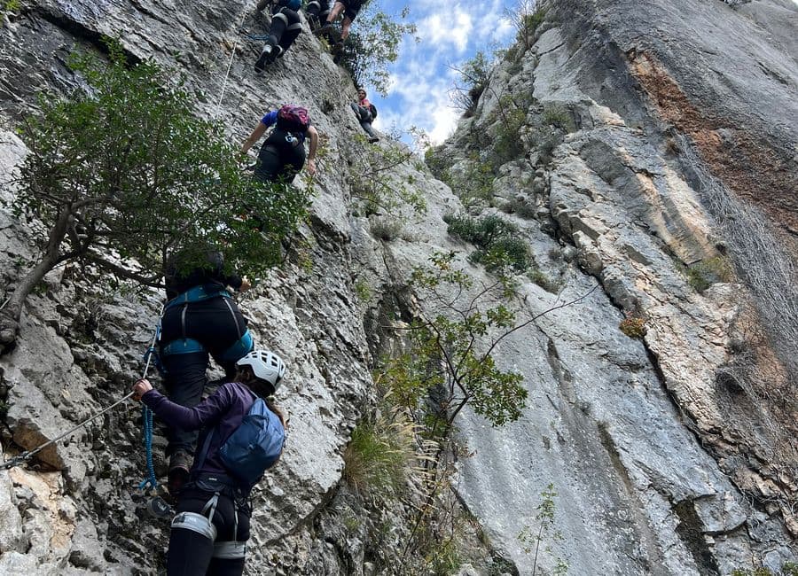 Group of climbers clipped to the cable on a steep limestone via ferrata, in helmets and harnesses