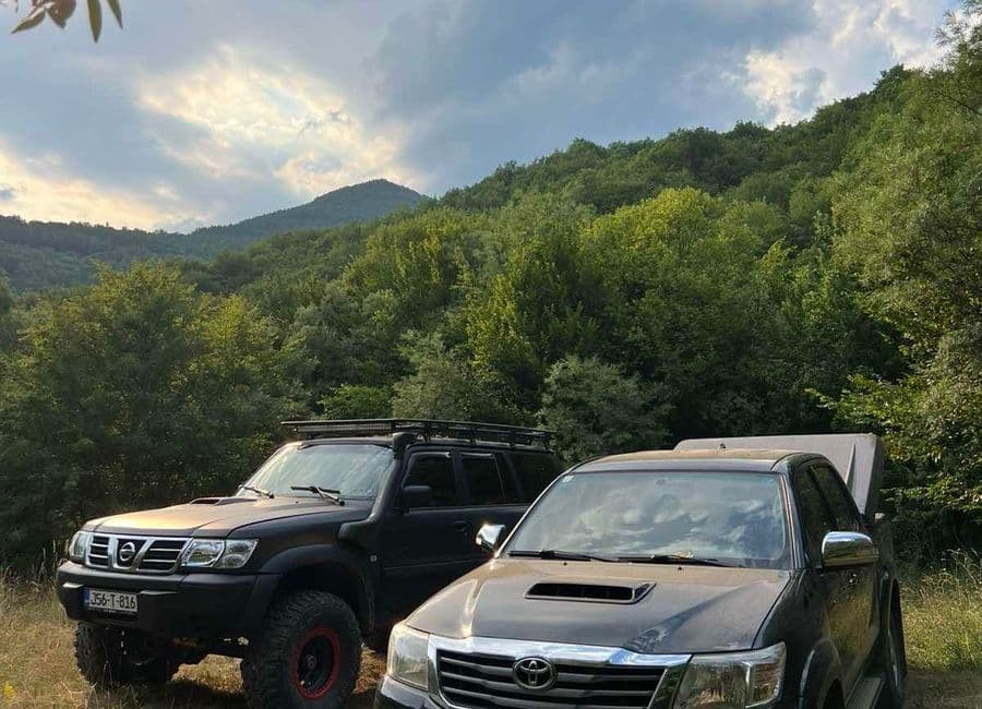 Two 4x4s parked at the edge of the forest below a wooded ridge on a Bosnian off-road route