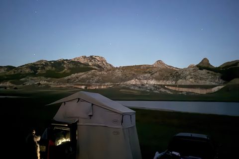 Roof tent pitched by a lake at dusk with bare karst peaks and the first stars above